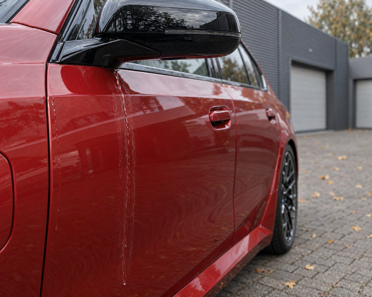 Detailing1 Auto trocknen — Nachlaufwasser aus dem Spiegel trocknet auf der Tür eines roten BMW M5 zu Kalkflecken ein