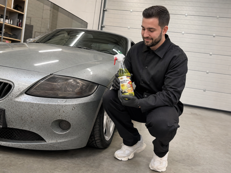 Daniel haelt die TUGA Chemie Insekten-Teufel Flasche vor der insektenverdreckten Front eines silbernen Sportwagens in der Detailing1 Warehouse — gezeigt im Artikel "Welcher Insektenentferner zu welcher Front passt"