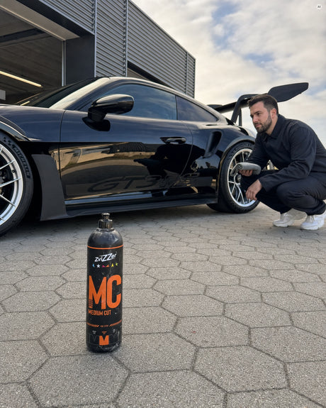 ZviZZer MC 3000 One-Step-Politur auf dem Pflaster vor der spiegelnd polierten Flanke eines schwarzen Porsche 911 GT3 RS.
