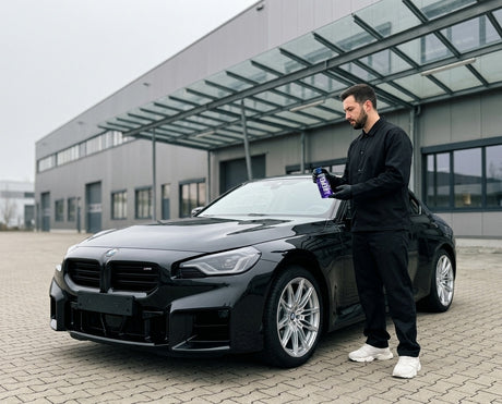 Daniel steht mit GYEON Q² View EVO Rain Repellent vor einem schwarzen BMW M2 vor der klaren Windschutzscheibe