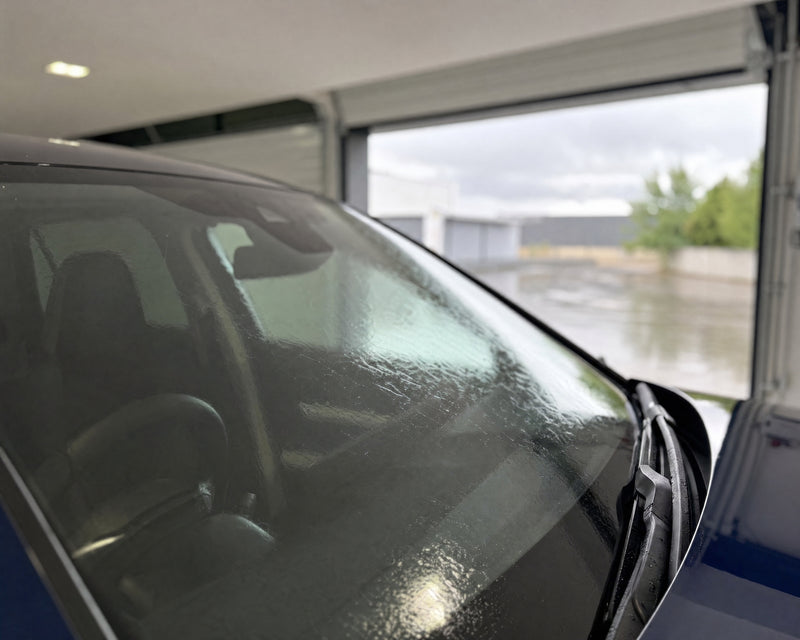 Regen läuft als flacher Wasserfilm über die Windschutzscheibe eines dunkelblauen Sportwagens — gezeigt im Artikel Scheibenver