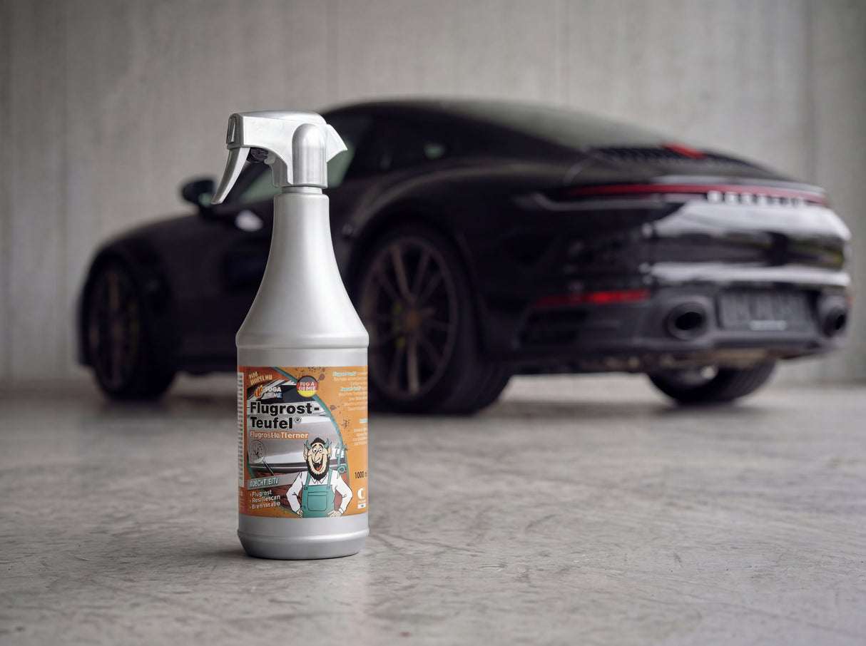 TUGA Chemie Flugrost-Teufel 1L Chrom-Sprühflasche mit orangem Label auf Betonvorplatz vor schwarzem Porsche 911